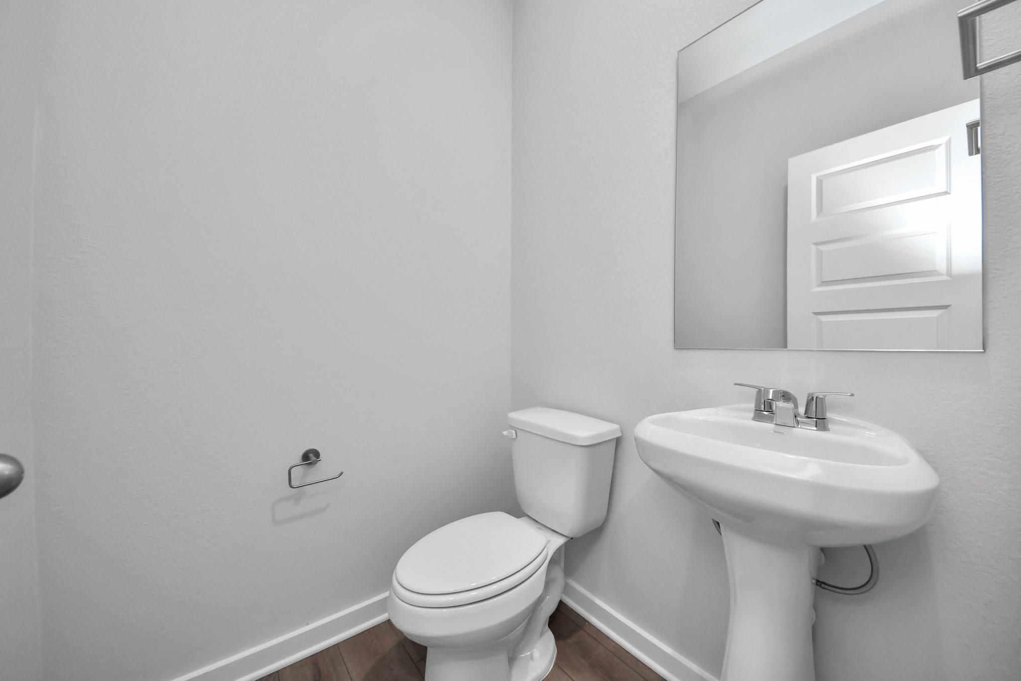 Modern half bath with pedestal sink and mirror in The Riviera A floor plan at Emberly, Beasley, Texas.