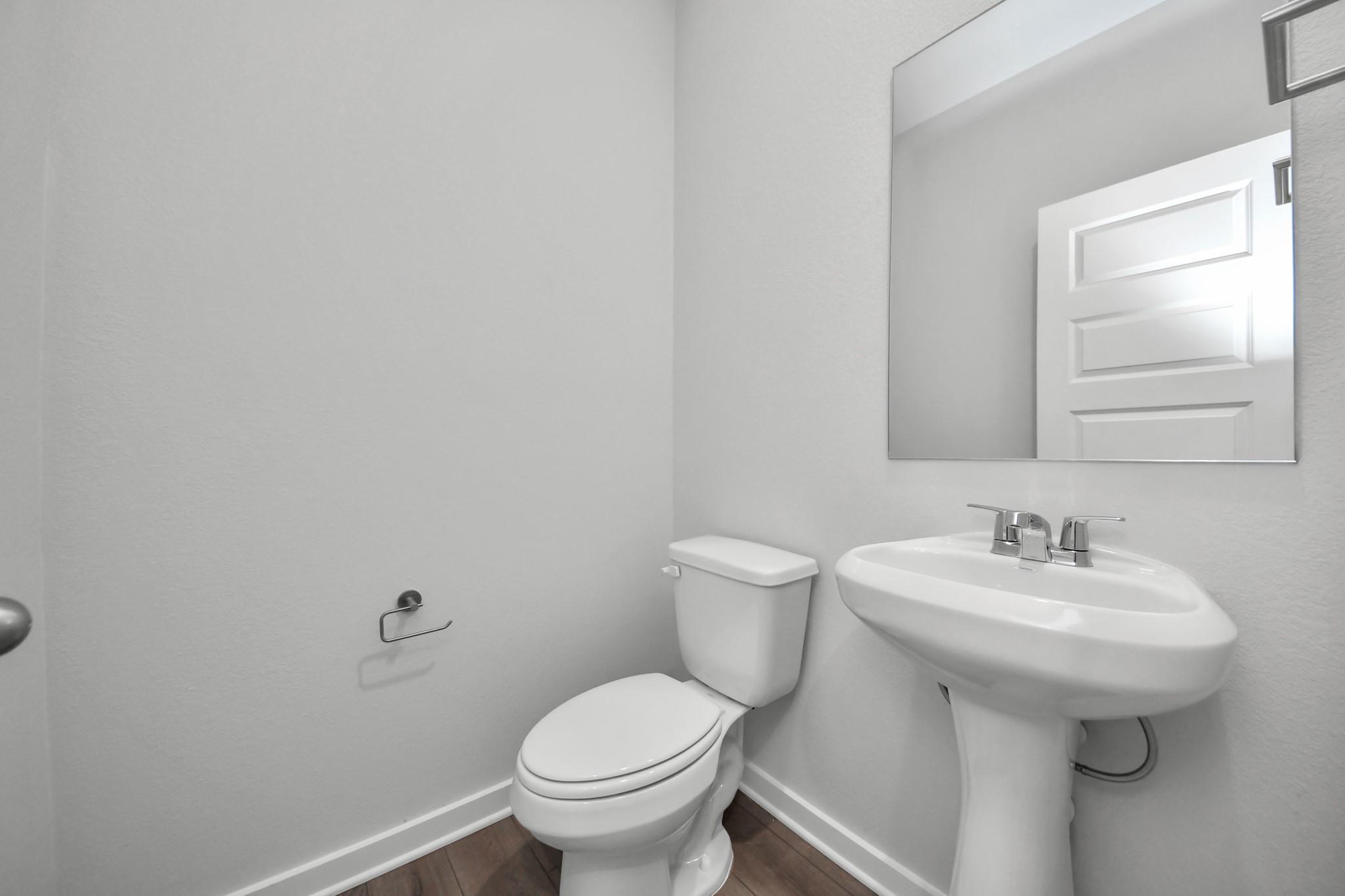 Modern half bath with pedestal sink and mirror in The Riviera A floor plan at Emberly, Beasley, Texas.