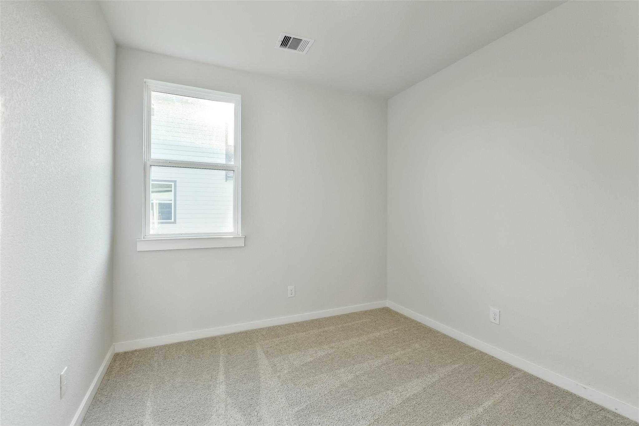 Spacious empty bedroom with beige carpet, white walls, and large window in Davidson Homes The Colorado F, Cleveland, Texas