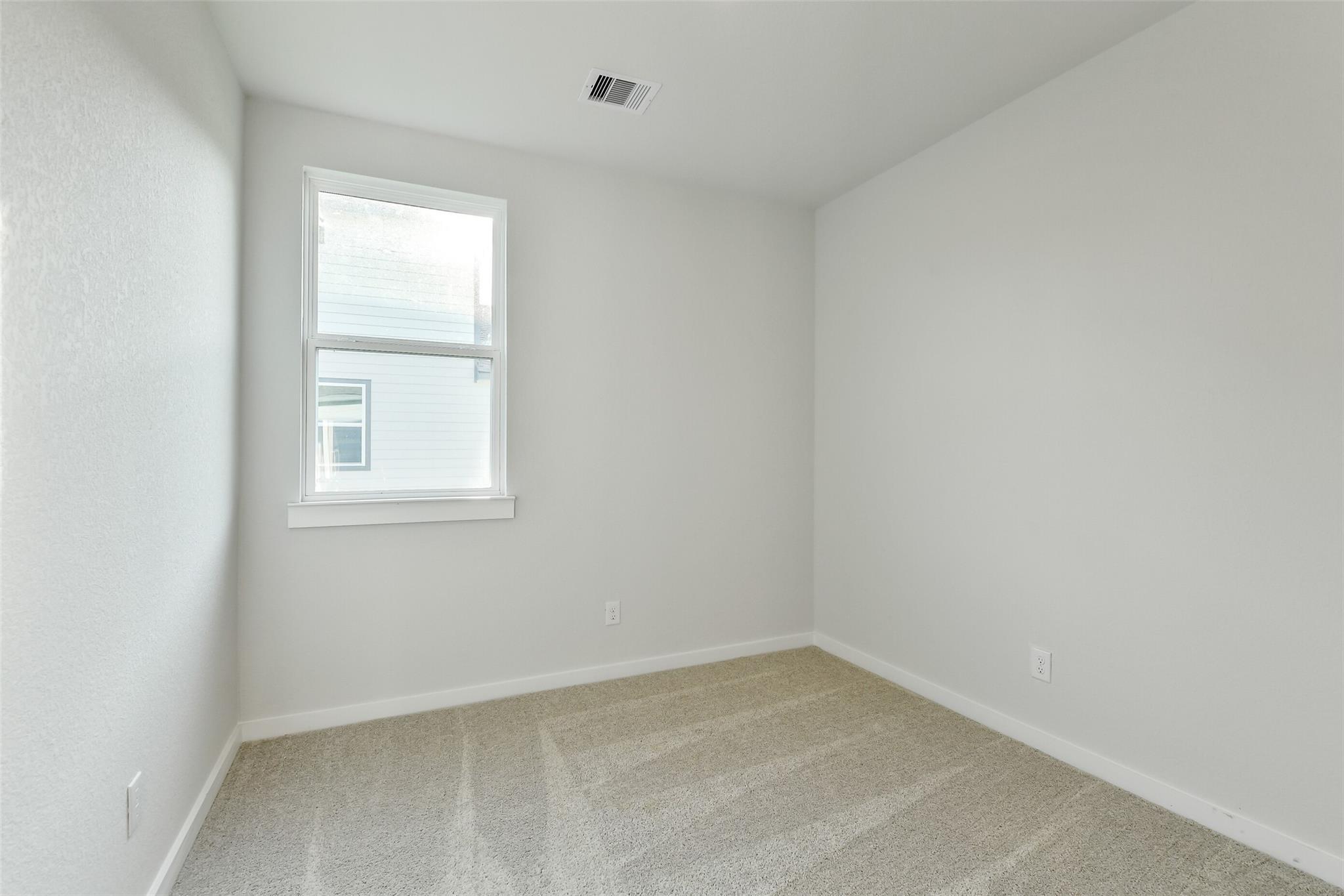 Empty secondary bedroom with beige carpet, white walls, and large window in Davidson Homes The Colorado F, Cleveland, Texas