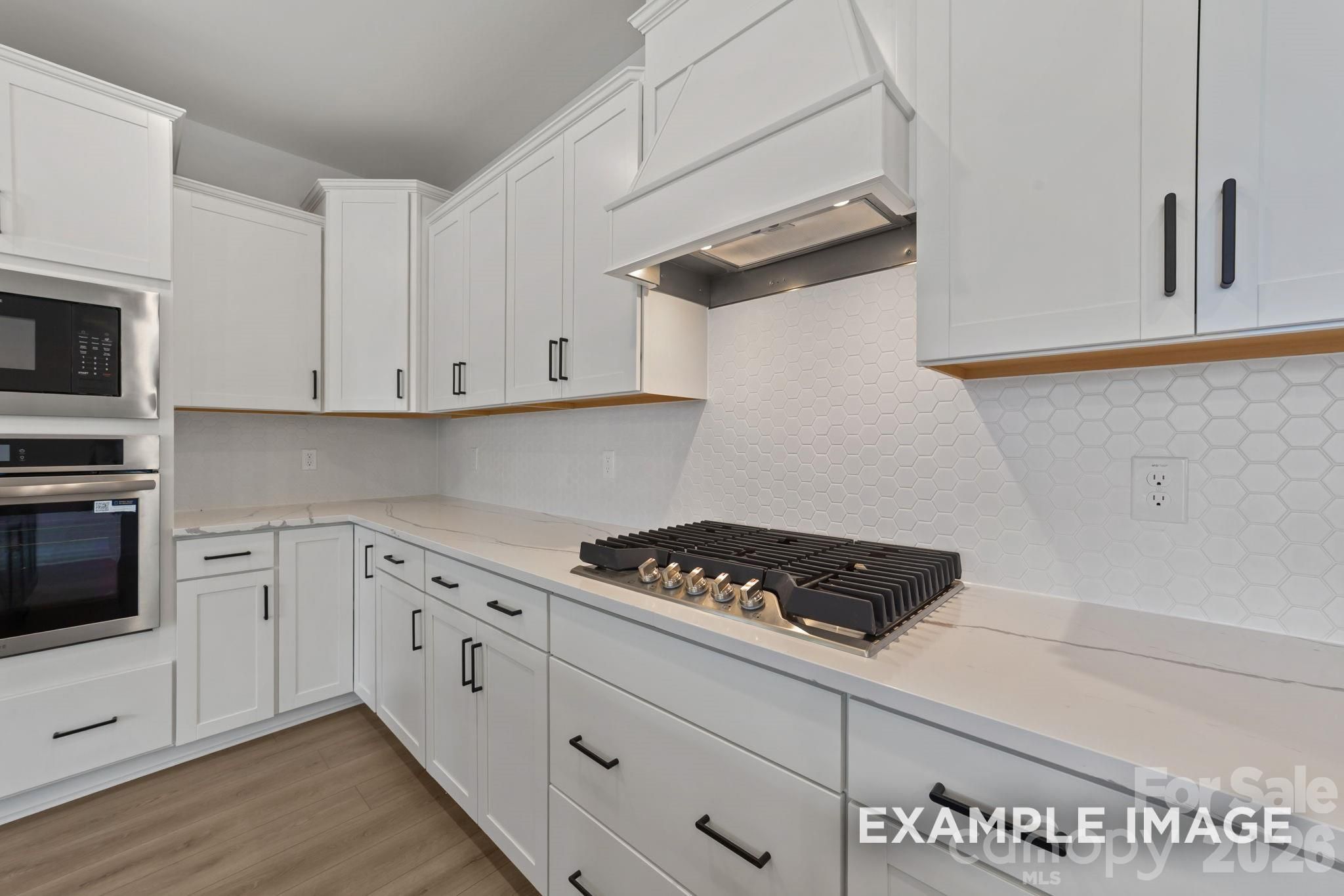 Modern kitchen with white shaker cabinets, gas cooktop, and tile backsplash in The Magnolia B home in Windgate, Mooresville.