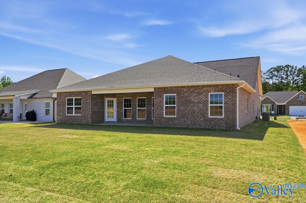 Rear view of brick 4-bedroom single-story home with covered patio, large windows, and green yard in Cain Park, Hartselle, Alabama