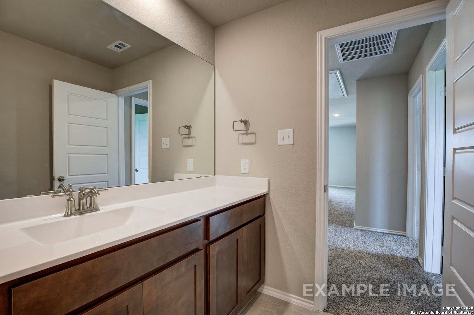 Modern bathroom vanity with single sink, large mirror, beige walls, and adjacent carpeted hallway in Davidson Homes The Murray K, San Antonio, Texas