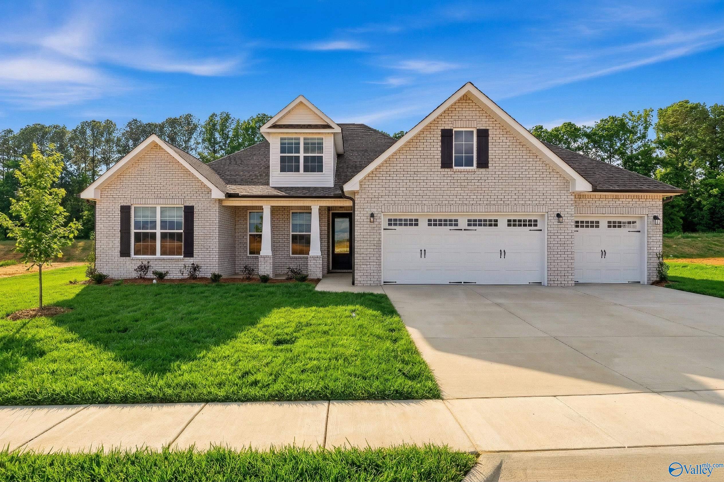 Brick 1.5-story Davidson Homes The Rockford with 3-car garage, covered porch, driveway, and lush lawn in Cain Park, Hartselle, Alabama