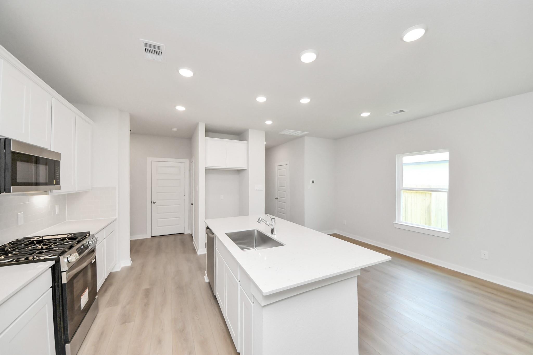 Modern kitchen with quartz island, white cabinetry, and stainless steel appliances in The Blanco E floor plan, Conroe, TX.