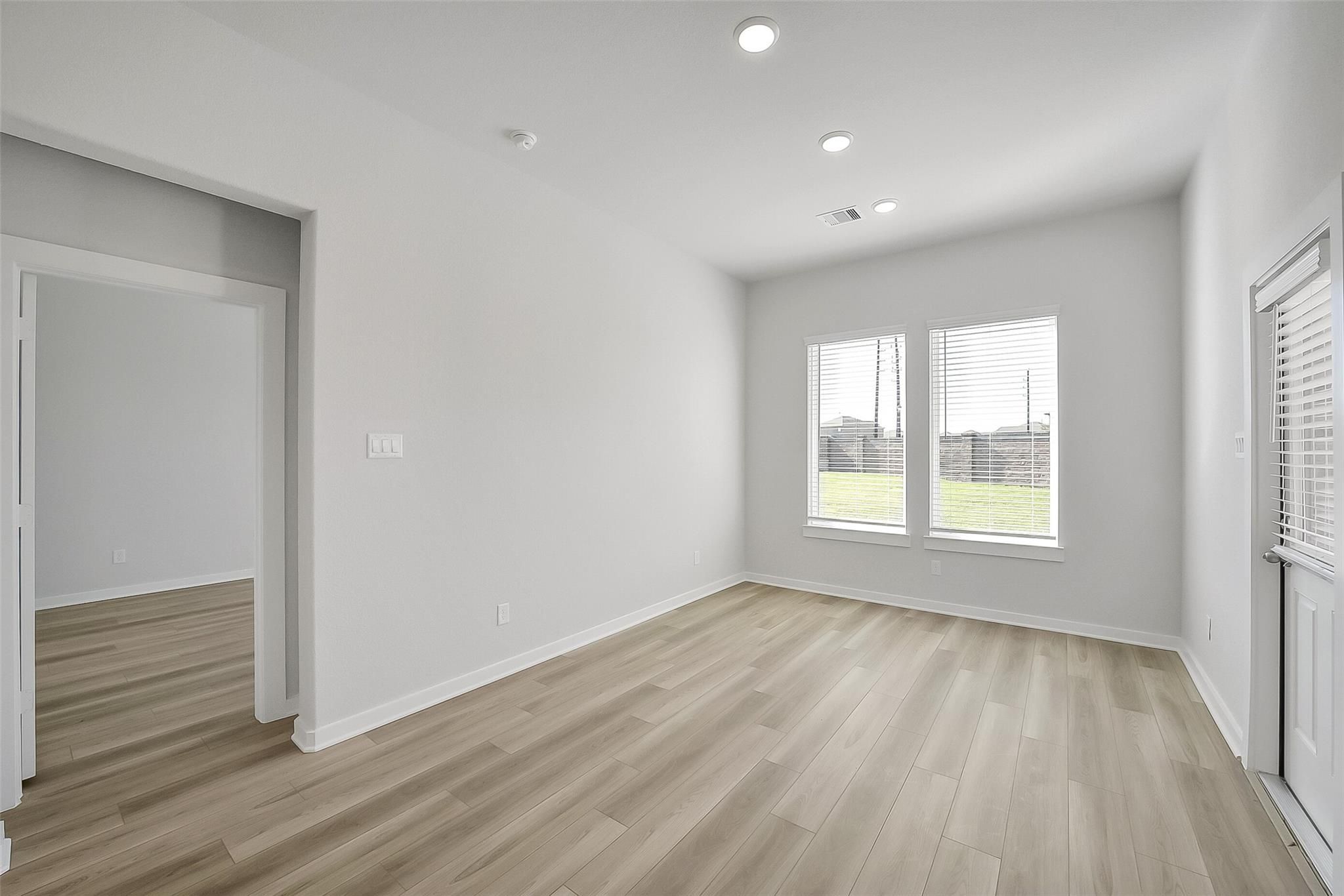 Bright bedroom with large windows overlooking green lawn, light wood floors in Davidson Homes The Acadia A, Katy Texas