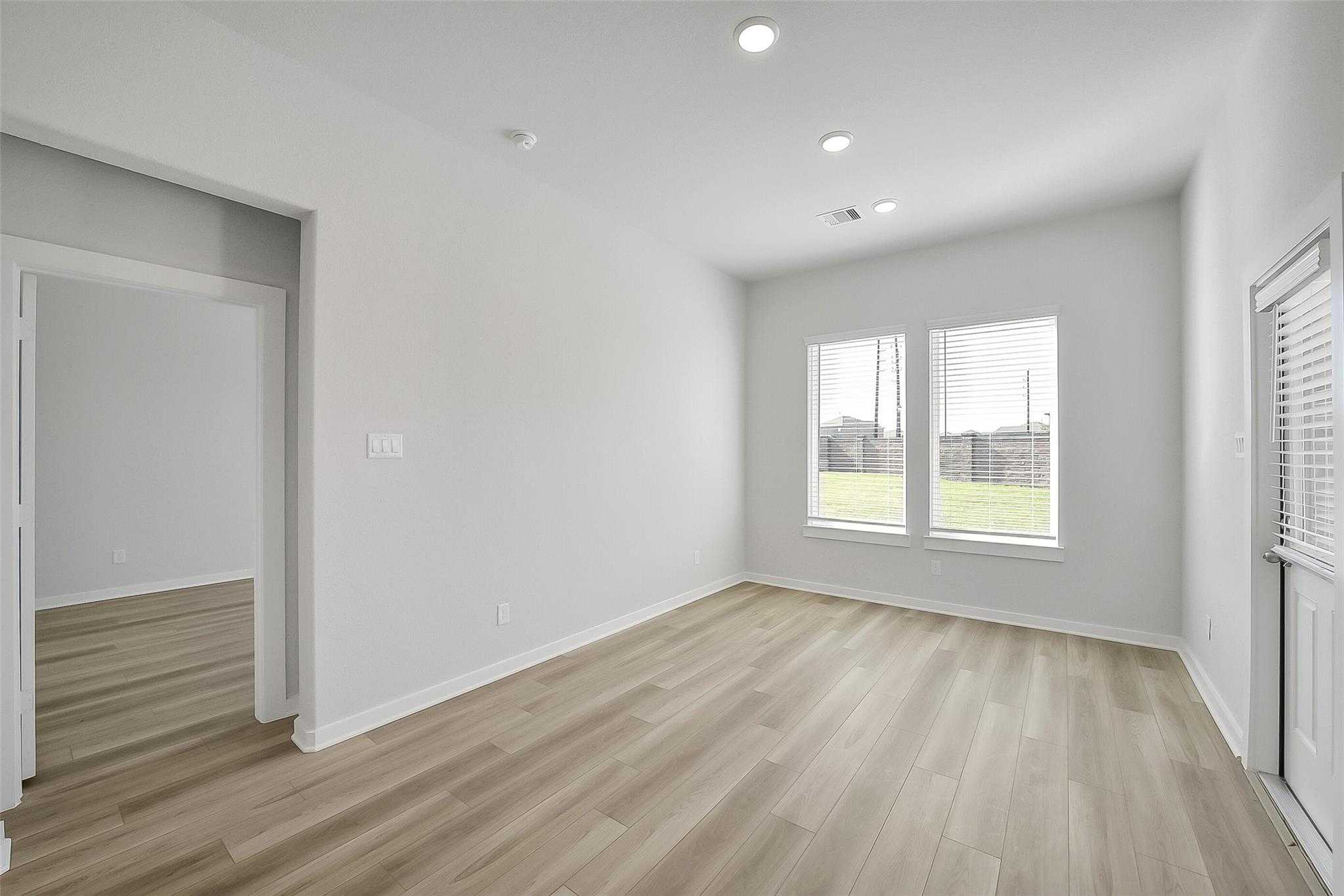 Bright bedroom with large windows overlooking green lawn, light wood floors in Davidson Homes The Acadia A, Katy Texas