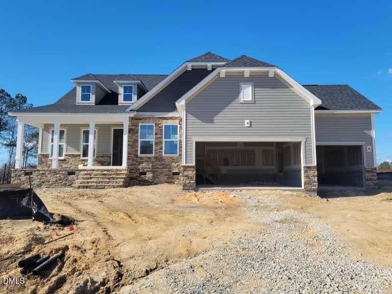 Modern gray stone-accented exterior of The Magnolia B 3-bedroom home with 3-car garage and covered porch in Tobacco Road, Angier, NC