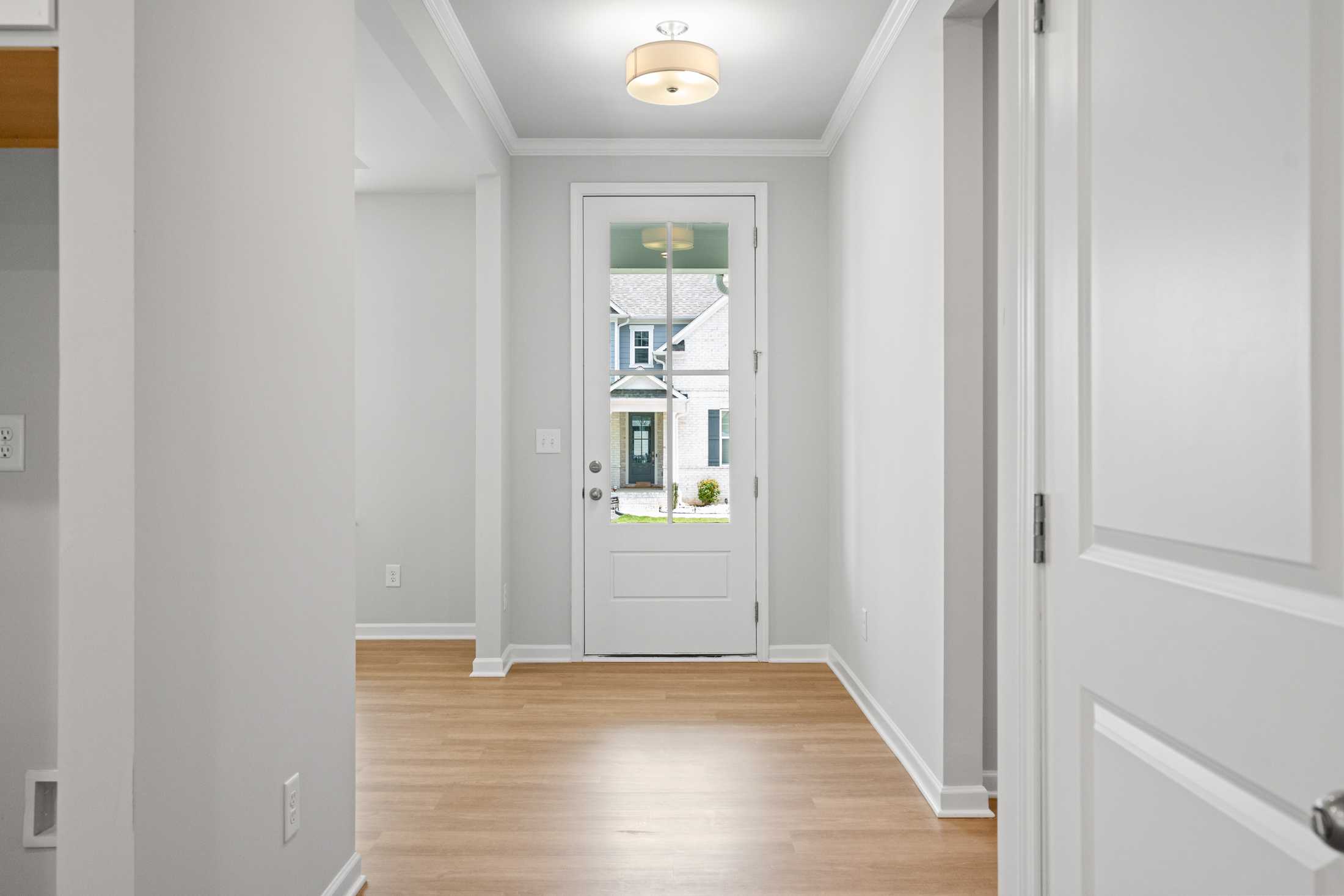 Spacious entryway in The Ash B at Wehunt Meadows with white walls, hardwood floors, and glass-front door view of Hoschton Georgia home exterior
