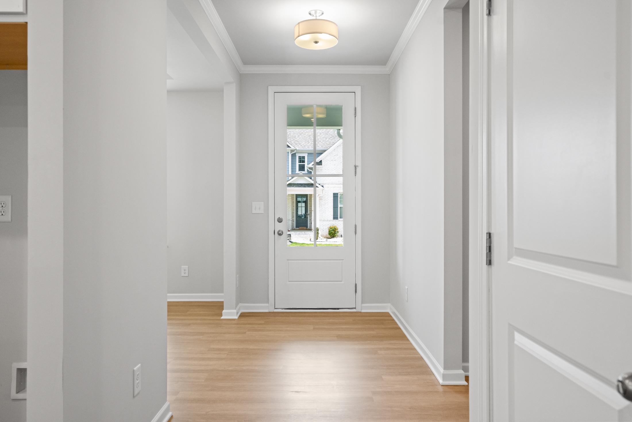Spacious entryway in The Ash B at Wehunt Meadows with white walls, hardwood floors, and glass-front door view of Hoschton Georgia home exterior