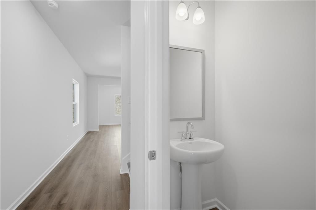 Bright half bath with pedestal sink and framed mirror beside hardwood-floored hallway in Davidson Homes The Russell B, Canton, GA