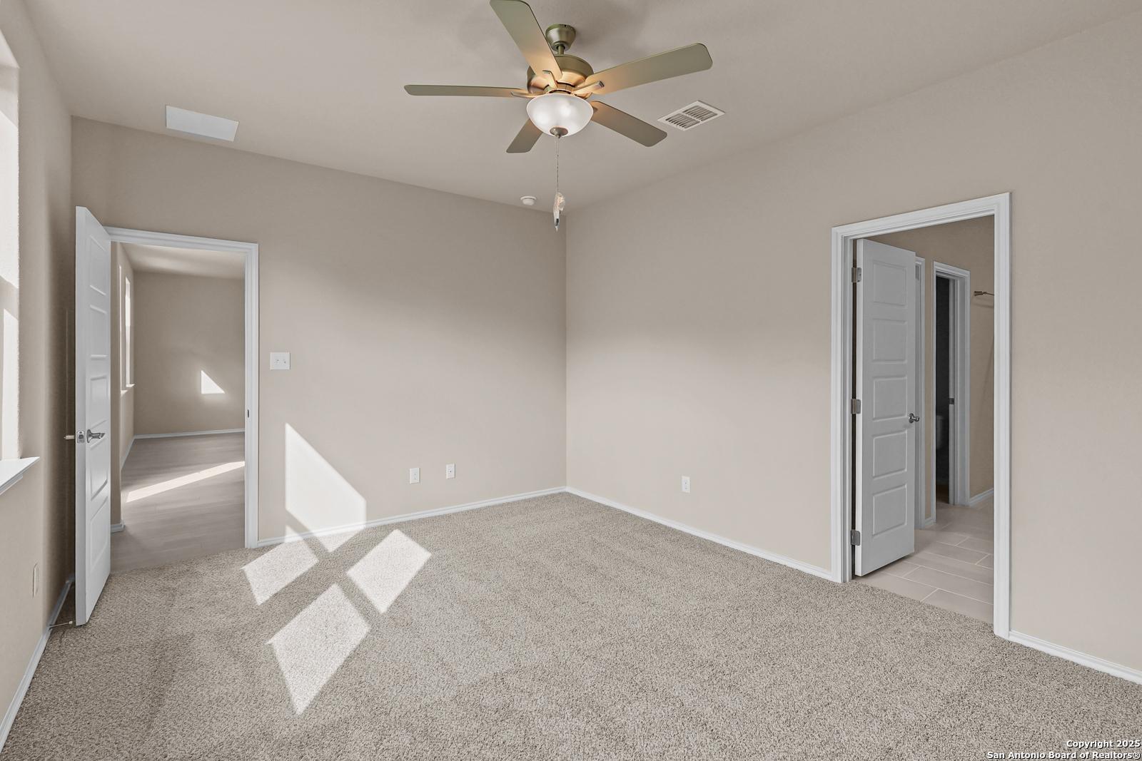 Bright secondary bedroom with beige carpet, ceiling fan, and open doorways in Davidson Homes The Douglas G, San Antonio, Texas