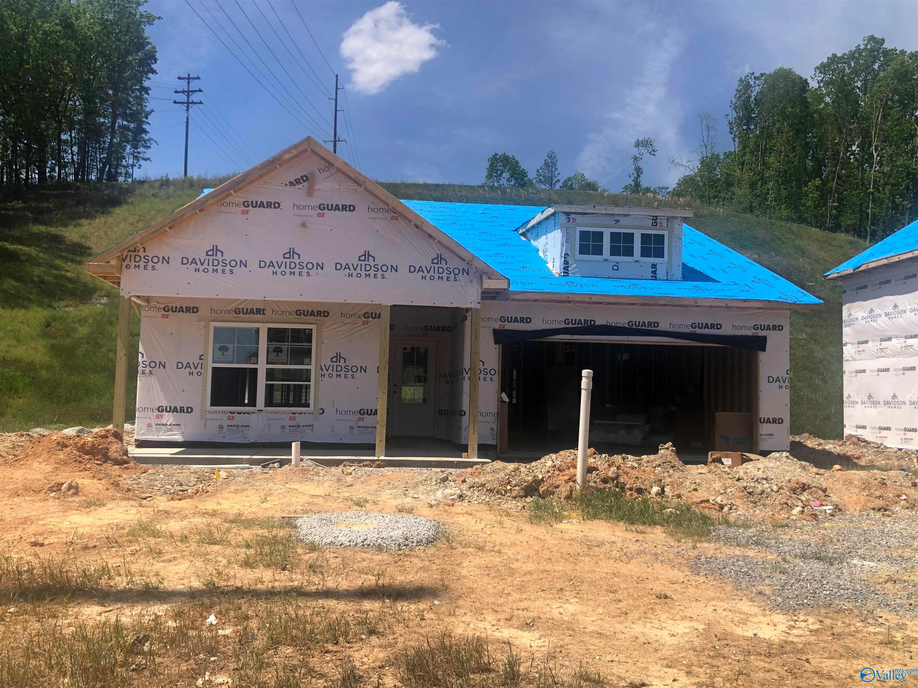 Under construction Davidson Homes Franklin E: single-story 3-bed frame with blue tarp roof, windows, 2-car garage in Noble Ridge, Cullman, AL