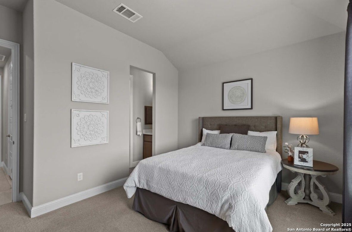 Cozy secondary bedroom with queen bed, en-suite bath, and gray walls in Davidson Homes The Garner B, Ladera, San Antonio