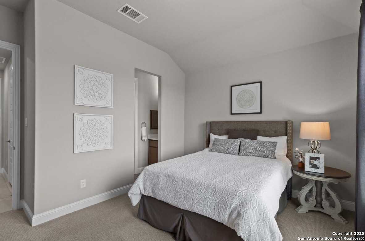 Cozy secondary bedroom with attached bath, queen bed, and gray walls in Davidson Homes The Garner B, Ladera, San Antonio