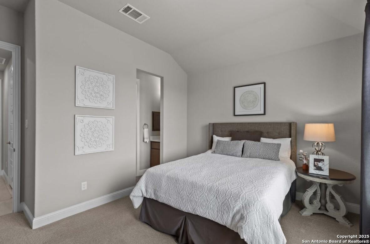 Cozy secondary bedroom with queen bed, en-suite bath, and gray walls in Davidson Homes The Garner B, Ladera, San Antonio