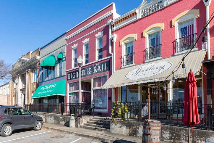 Historic downtown Opelika Alabama street with colorful storefronts, High & Rail Gallery, green awnings, and red umbrella patio near Anderson Lakes