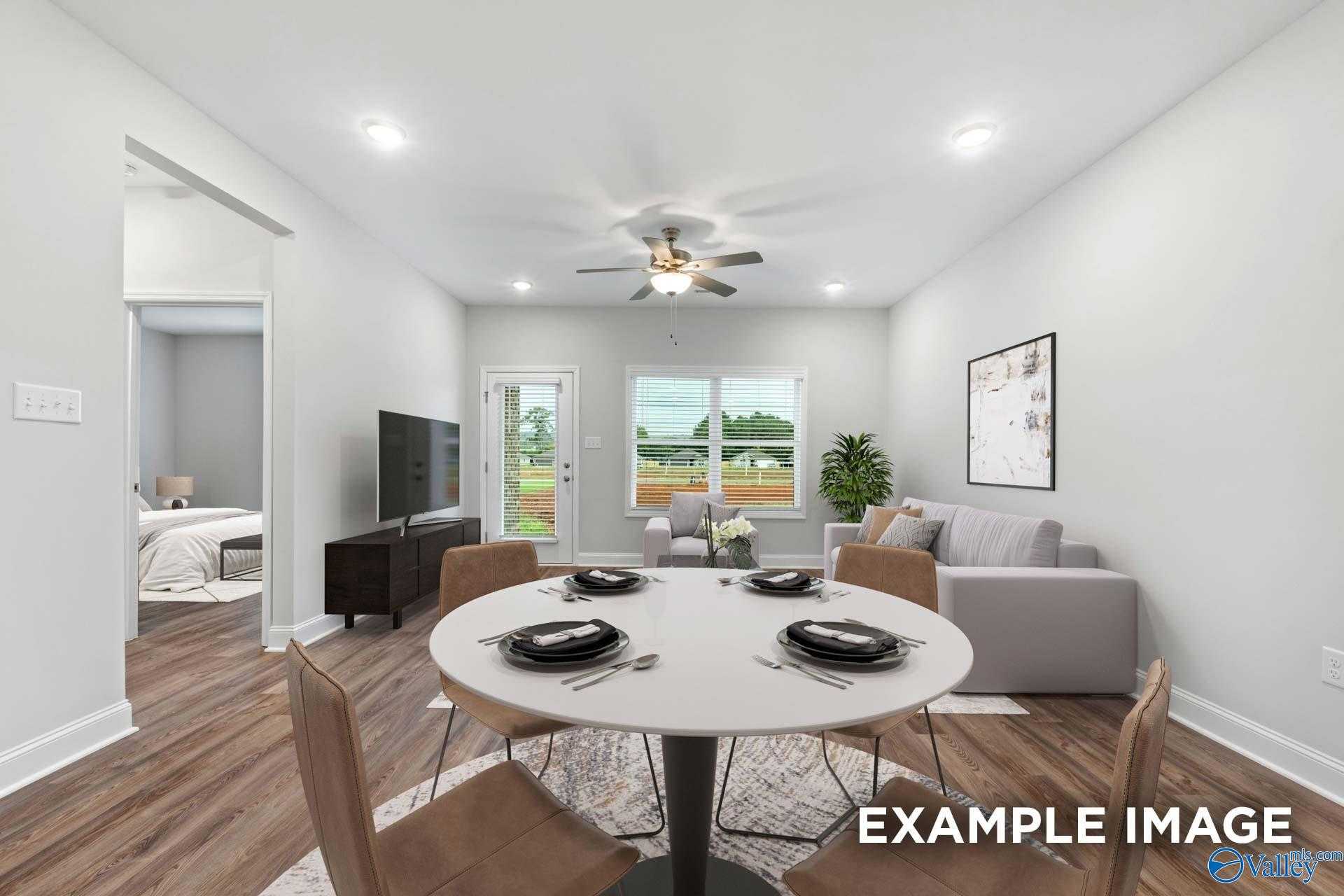 Open living-dining area with round table, gray sofa, TV, and backyard view in The Cumberland 3-bedroom home, Decatur, Alabama