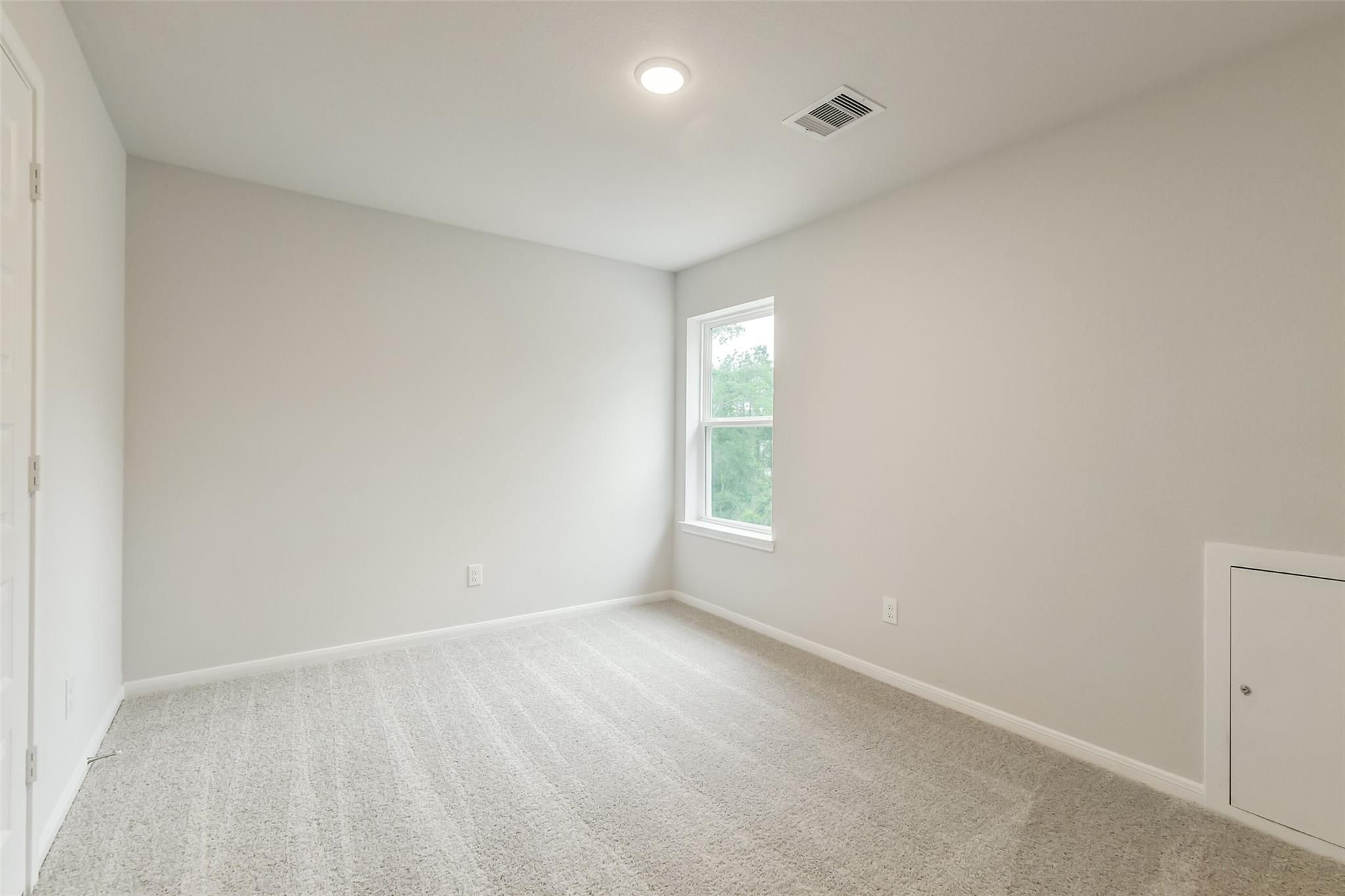 Bright secondary bedroom featuring neutral gray walls, carpeted floor, and large window in Davidson Homes The Brazos F, Conroe, Texas