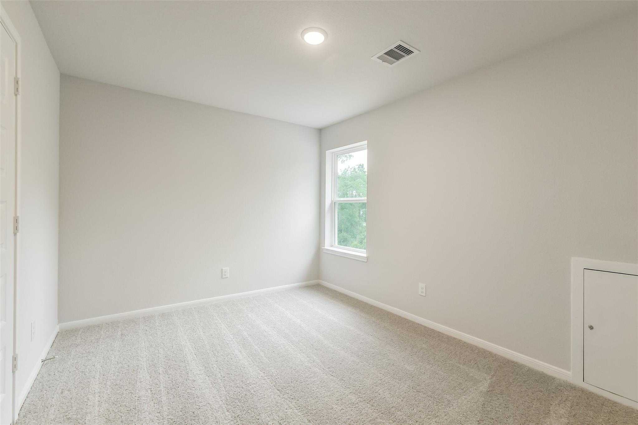 Bright secondary bedroom featuring neutral gray walls, carpeted floor, and large window in Davidson Homes The Brazos F, Conroe, Texas