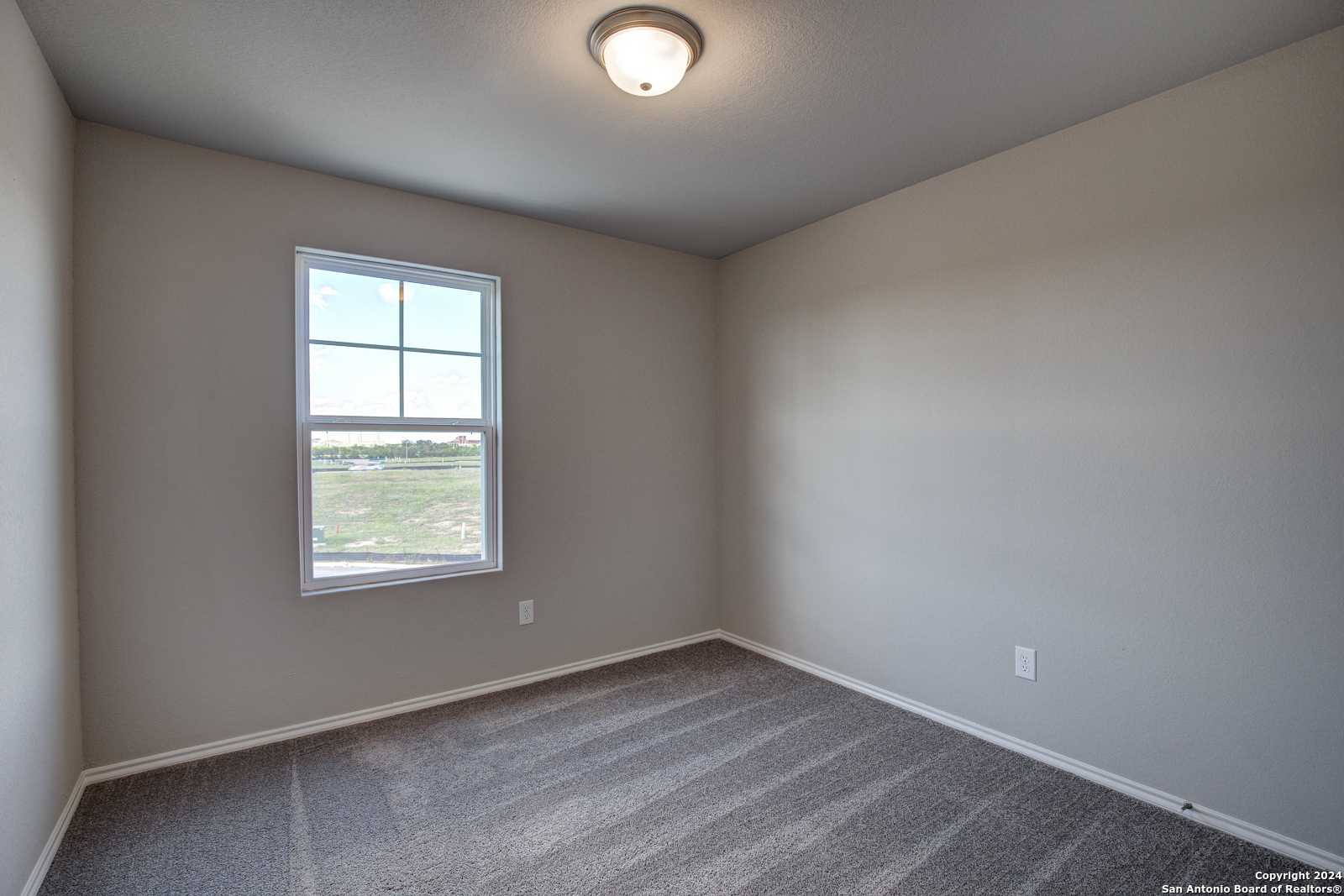 Cozy bedroom with beige walls, plush carpet, and large window overlooking open fields in Davidson Homes The Blanco C, San Antonio