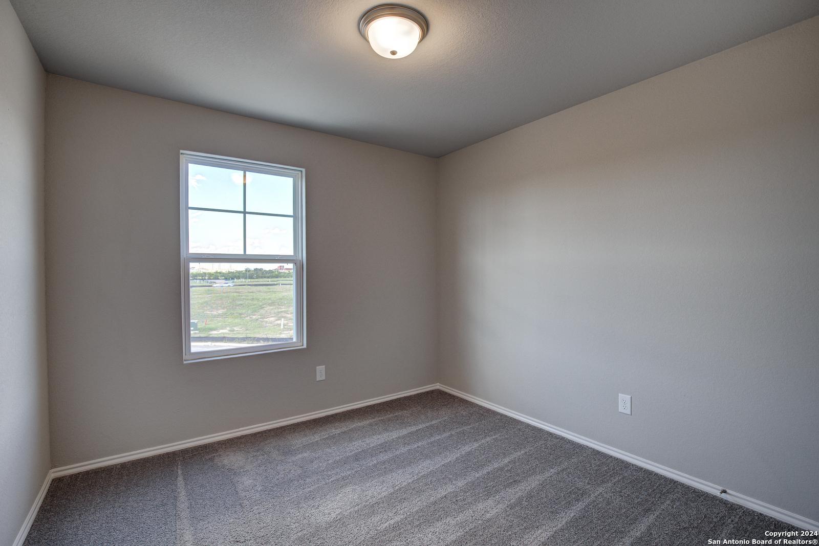 Bright bedroom with neutral beige walls, plush carpet floor, and window view of open fields in Davidson Homes The Blanco C, San Antonio