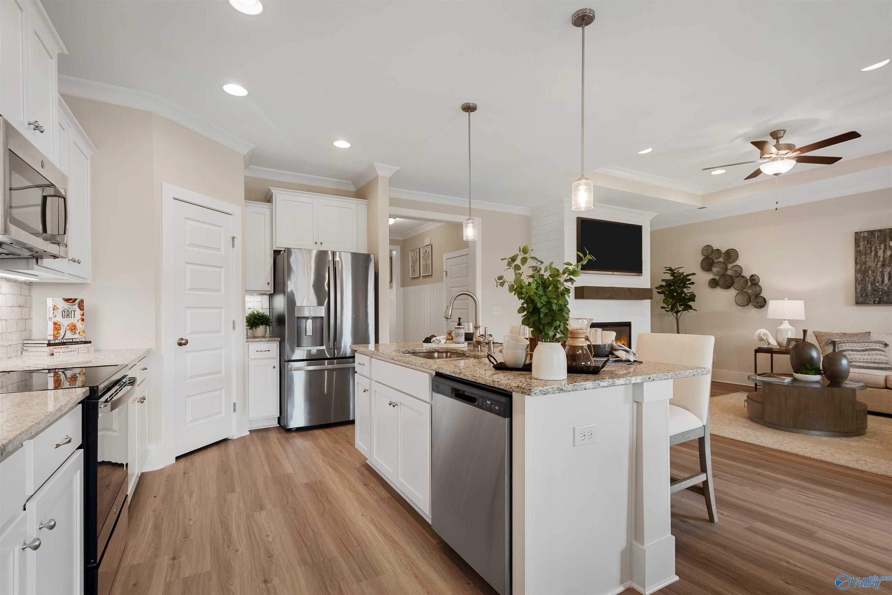 Open-concept kitchen with white cabinets, stainless appliances, and island bar flowing into living room with fireplace, The Everett by Davidson Homes, New Market AL