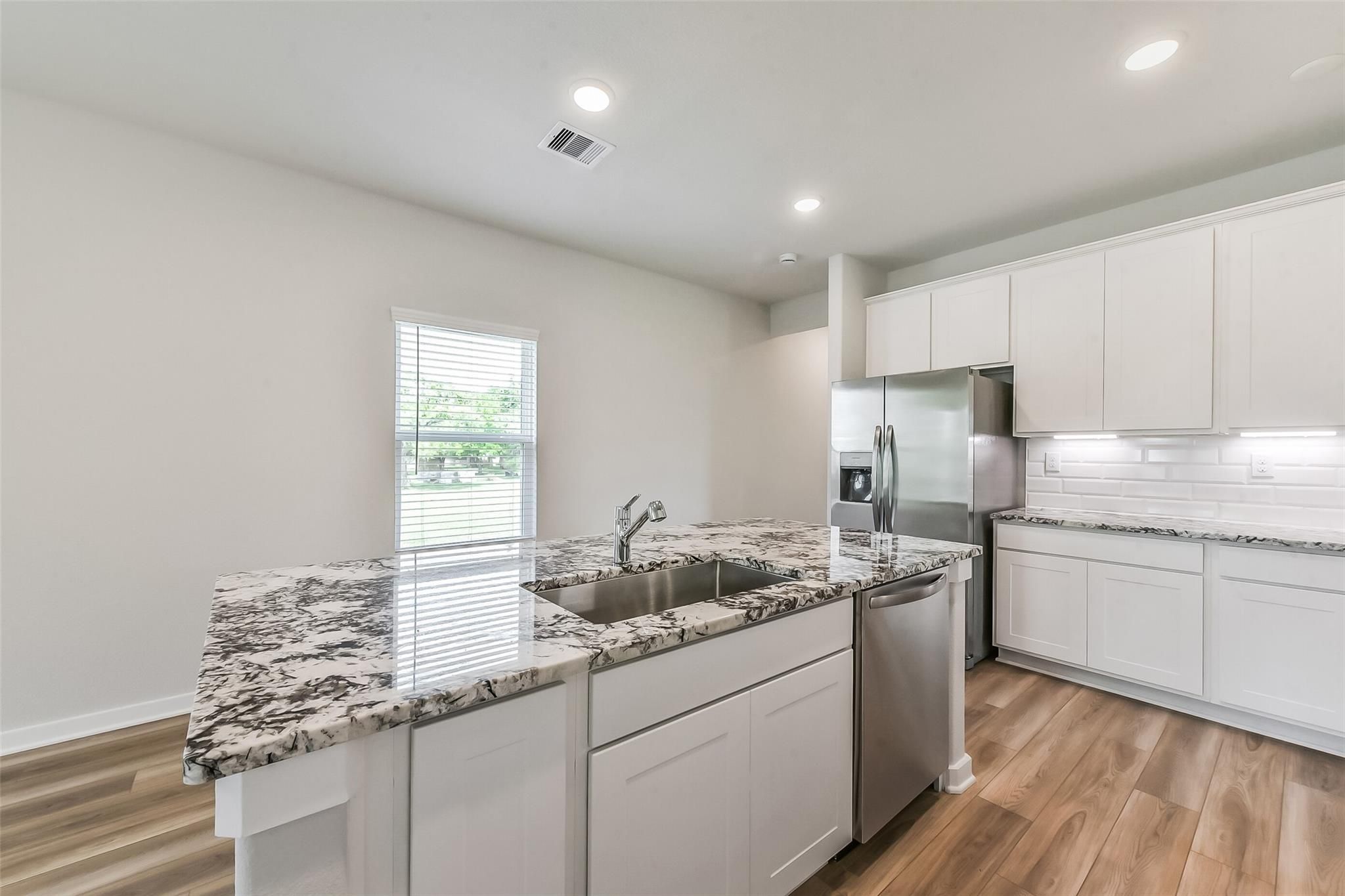 Modern kitchen with white shaker cabinets, swirled granite island sink, stainless steel appliances, subway tile backsplash in Davidson Homes The Frio G, Magnolia TX