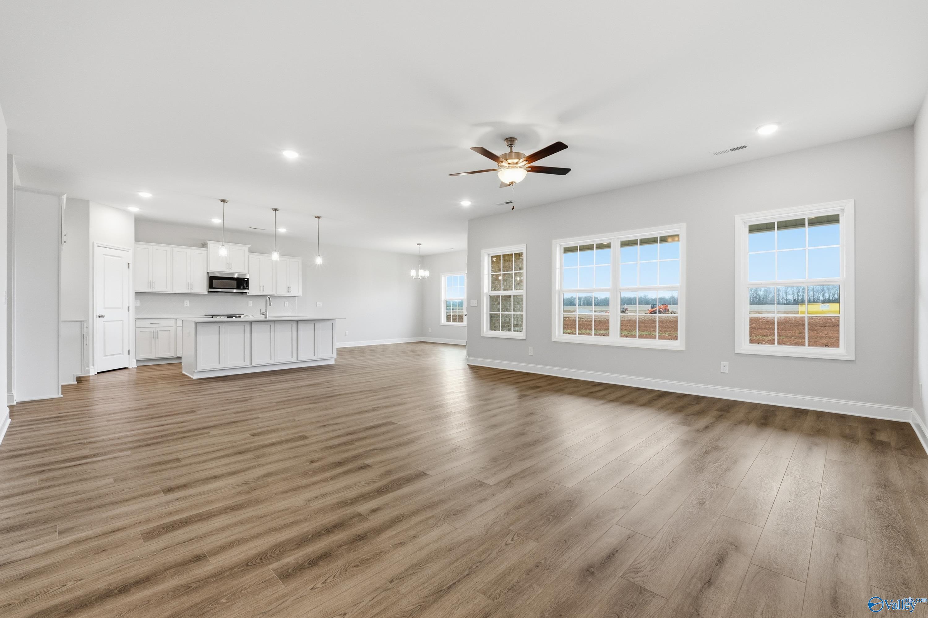 Open-concept kitchen-living area with white cabinets, island, ceiling fan, large windows, and hardwood floors in Davidson Homes The Rockford, Meridianville, AL