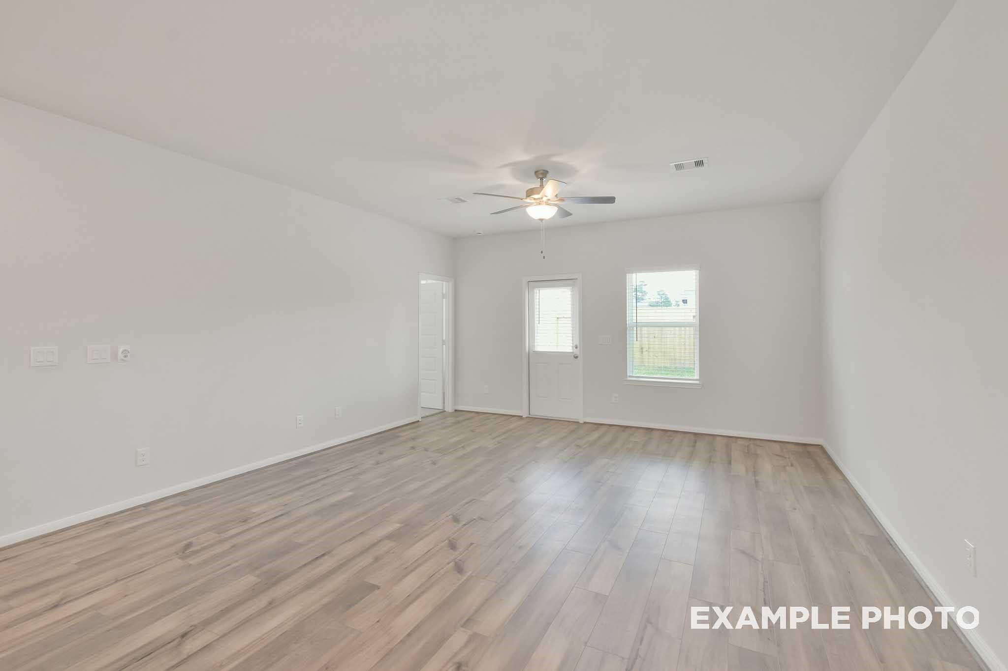Bright open living room with luxury vinyl plank flooring, ceiling fan, and rear door in Davidson Homes' Brazos E plan, Conroe, TX