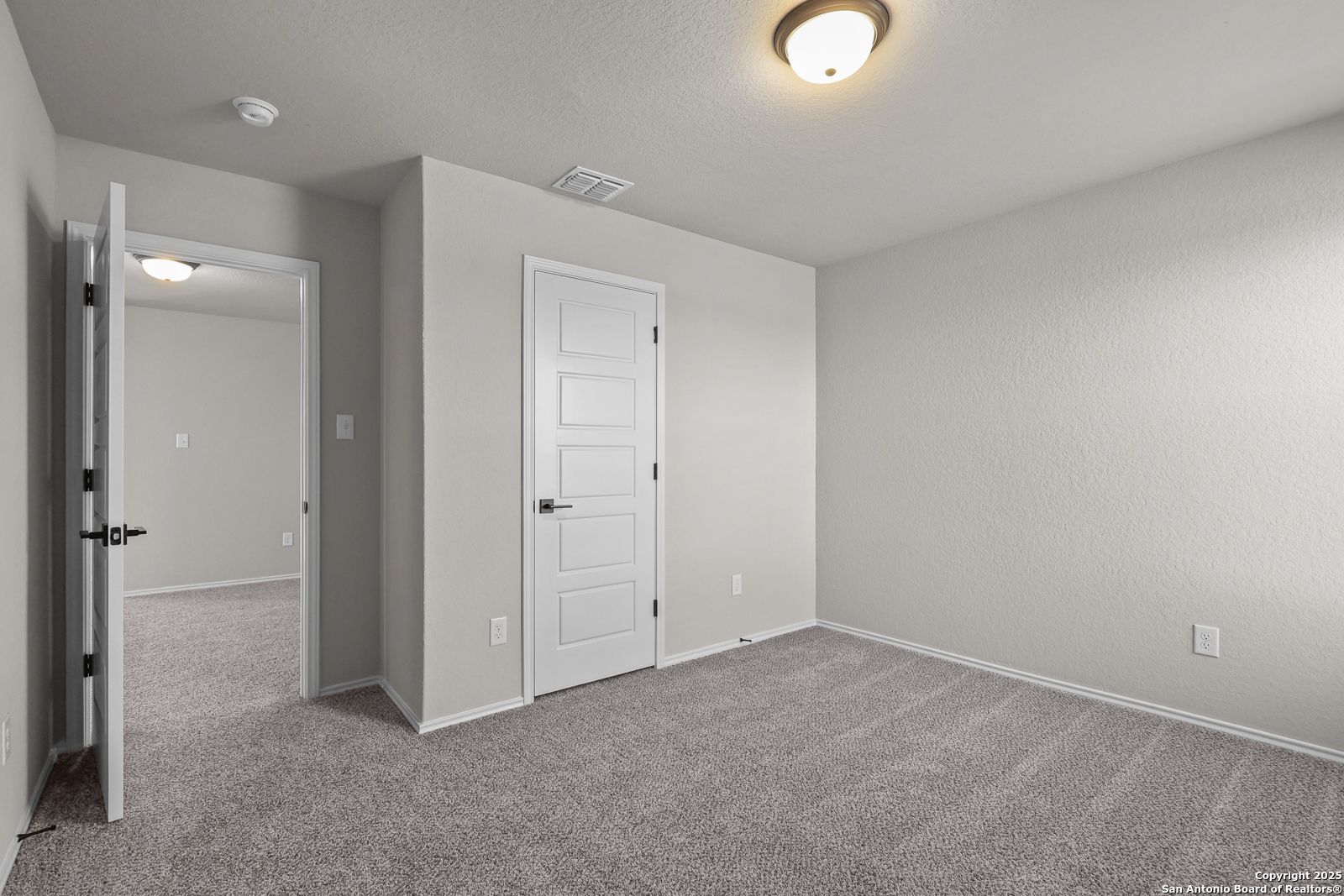 Empty bedroom with neutral beige walls, gray carpet, and open closet door in Davidson Homes The Brazos C, San Antonio