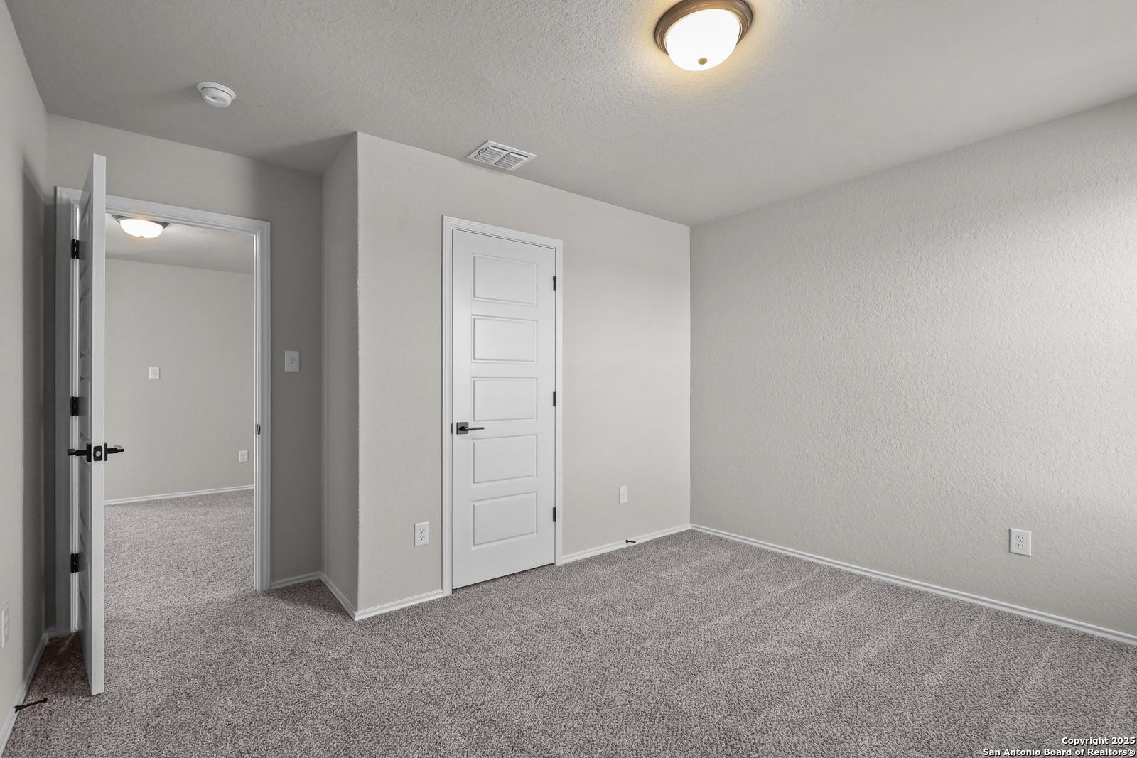 Empty bedroom with neutral beige walls, gray carpet, and open closet door in Davidson Homes The Brazos C, San Antonio