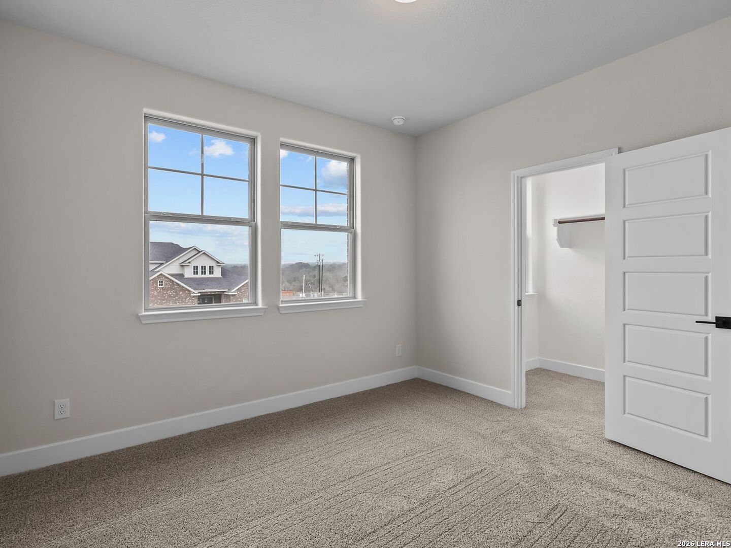 Bright bedroom with neutral carpet and walk-in closet in The Belmont H floor plan at Potranco Oaks, Castroville, Texas.