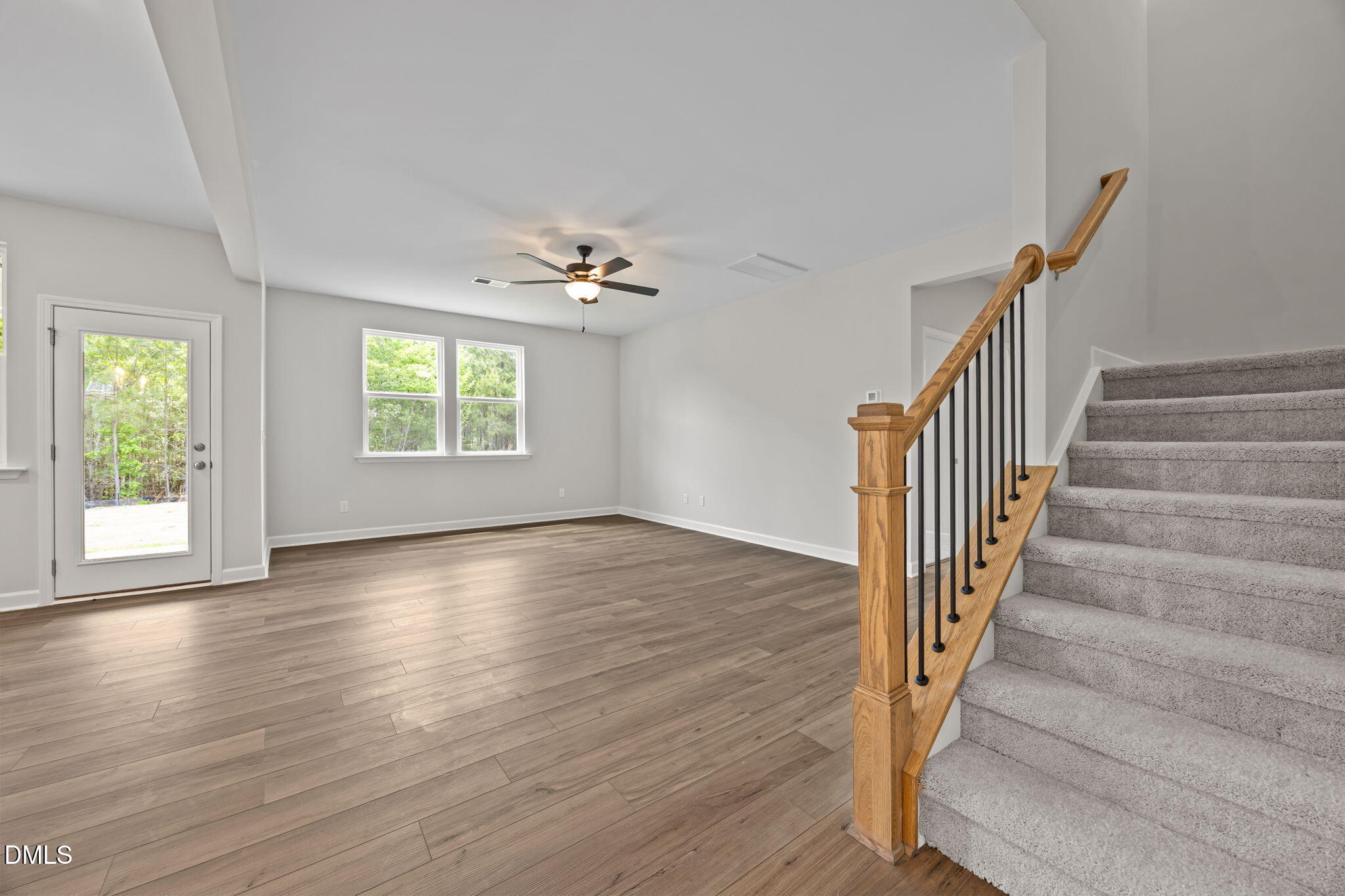 Bright open foyer with light hardwood floors, large windows showing greenery, ceiling fan, and oak staircase in Davidson Homes The Willow D, Wendell, NC