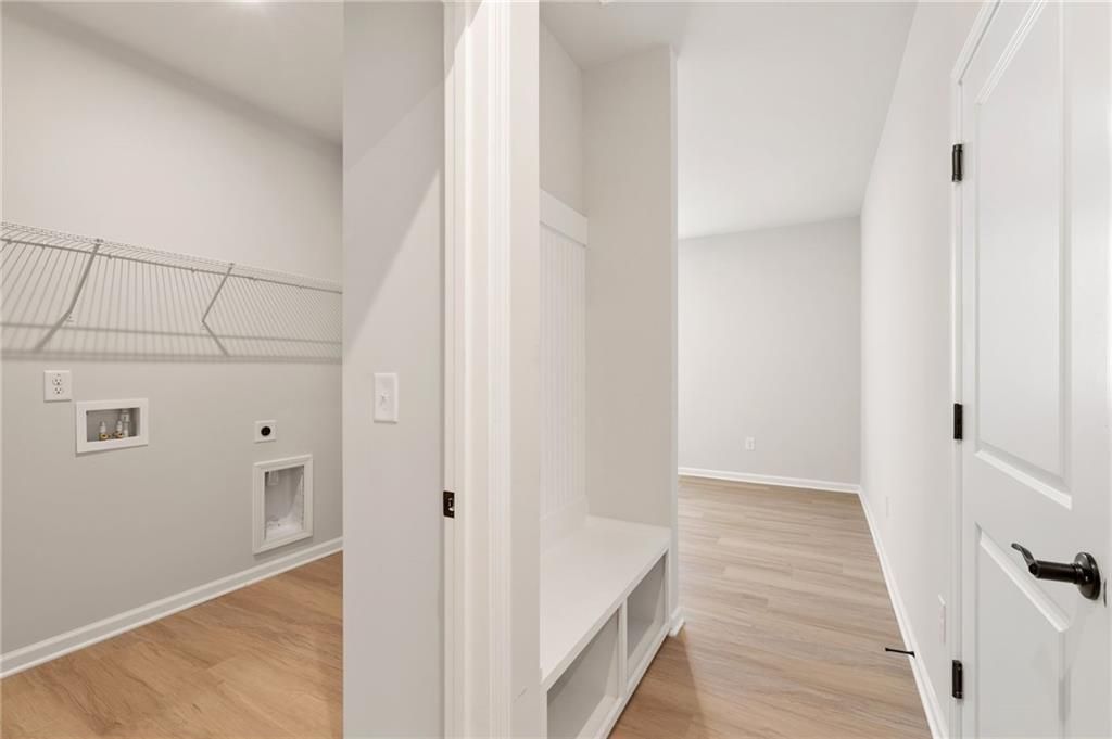 Bright laundry room with wire shelving, built-in bench, and hardwood floors in Davidson Homes The Daphne C, Loganville, GA
