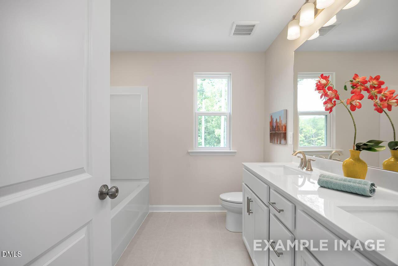 Modern bathroom with white double vanity, bathtub, toilet, and red orchids in Davidson Homes The Willow D, Lillington, NC