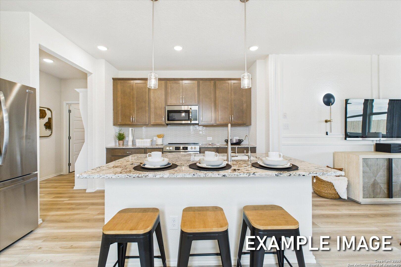 Modern open-concept kitchen with white quartz island, stainless appliances, and wood stools in Davidson Homes The Brazos C, San Antonio