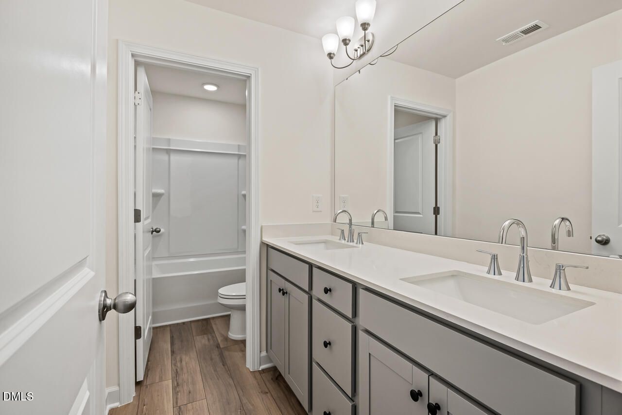 Dual-sink bathroom with gray vanity, white countertops, and tub-shower combo in Davidson Homes The Hickory II B, Lillington NC