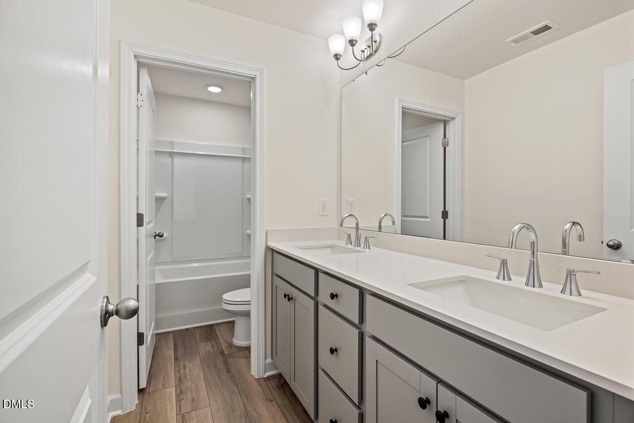 Dual-sink bathroom with gray vanity, white countertops, and tub-shower combo in Davidson Homes The Hickory II B, Lillington NC