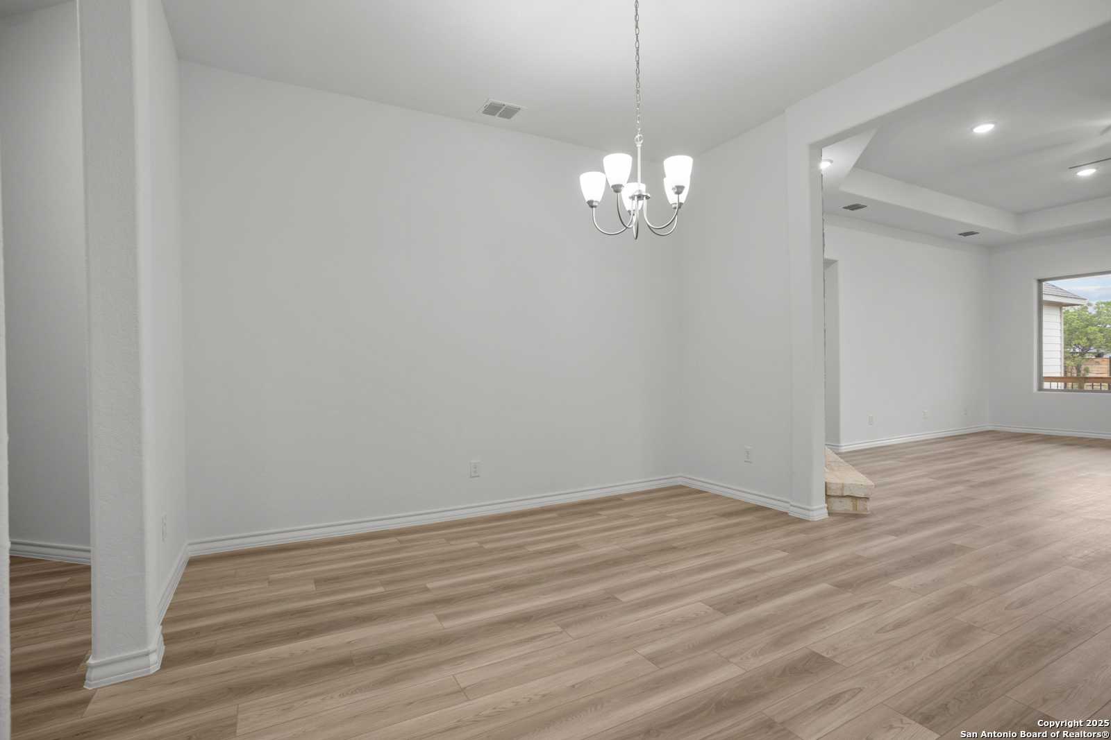 Formal dining room with elegant chandelier, white walls, hardwood floors, and large window in Davidson Homes Summerlin B, Castroville, Texas