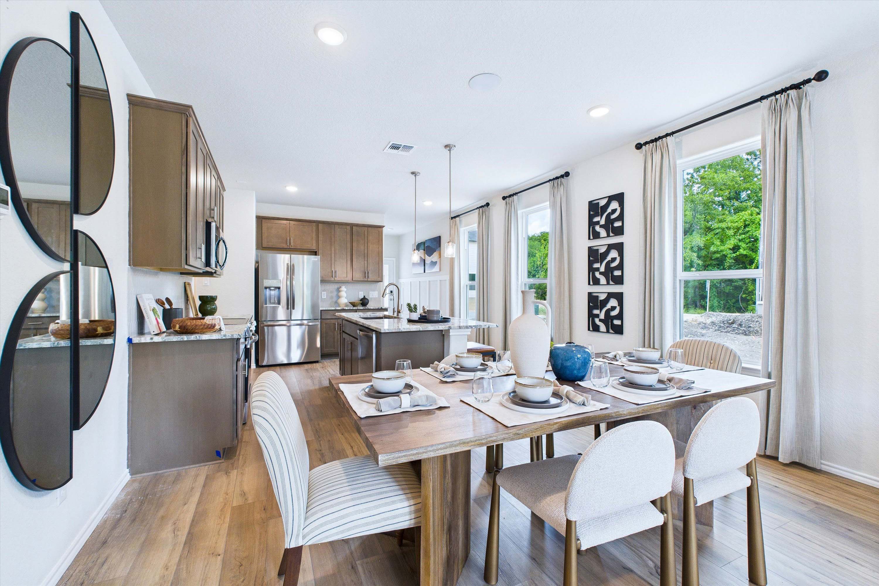 Open-concept dining area and kitchen in The Gillian C featuring wood cabinets, stainless appliances, and a modern island.