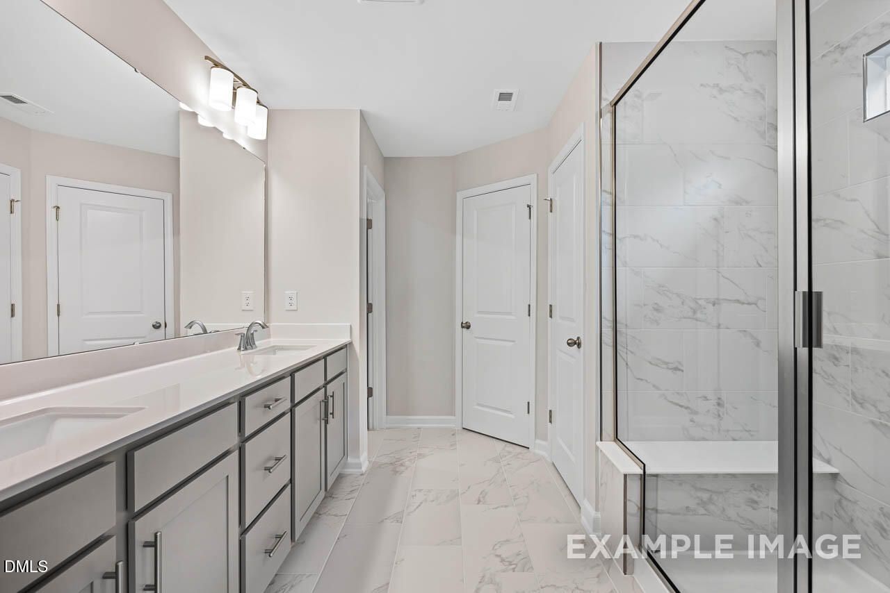 Modern master bathroom featuring double vanity, frameless glass shower with marble tiles and bench in Davidson Homes The Chestnut B, Lillington, NC