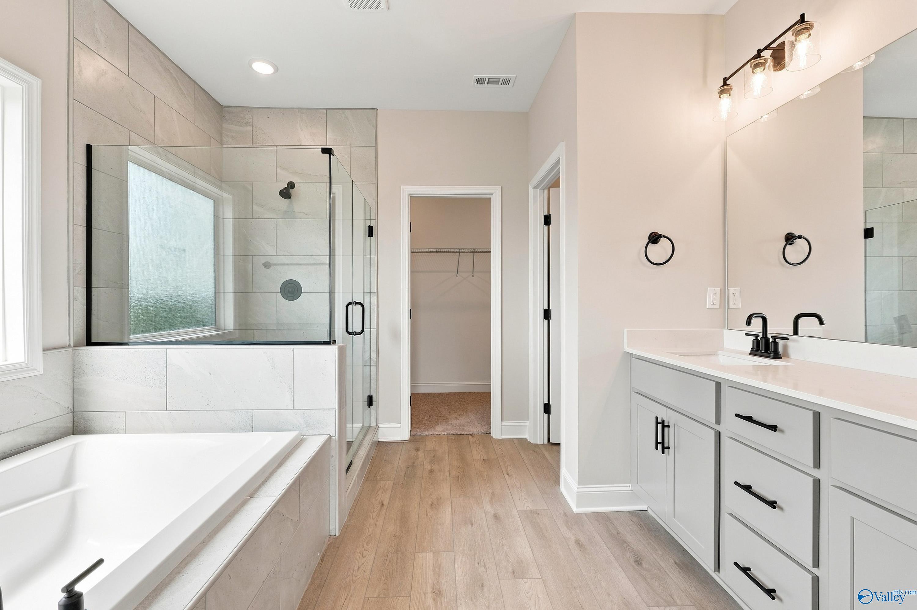Modern master bathroom with soaking tub, glass walk-in shower, dual vanity, and wood-look flooring in Athens, Alabama home