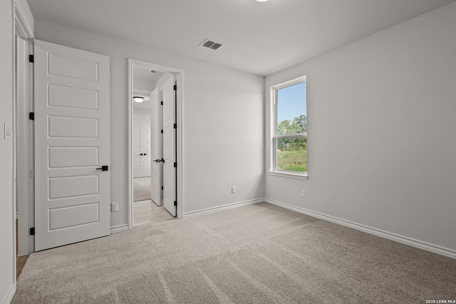 Bright carpeted bedroom with white paneled doors and window overlooking greenery in Davidson Homes The Oxford F, Castroville, TX