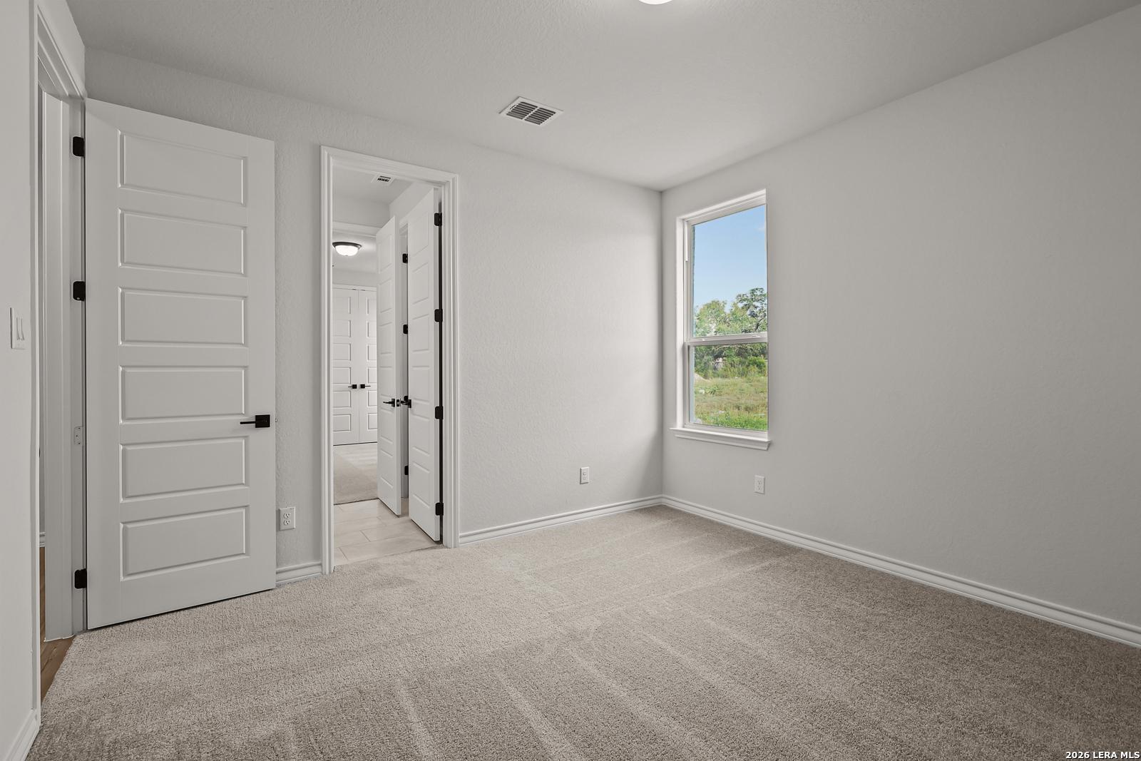 Bright carpeted bedroom with white paneled doors and window overlooking greenery in Davidson Homes The Oxford F, Castroville, TX