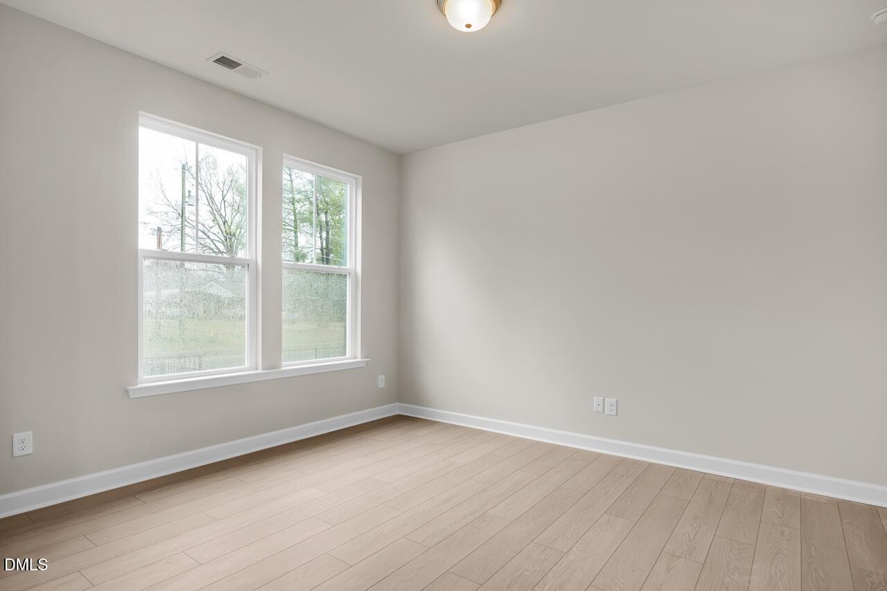 Bright empty bedroom with light gray walls, large double windows with wooded view, oak hardwood floors in Davidson Homes The Avery, Knightdale NC