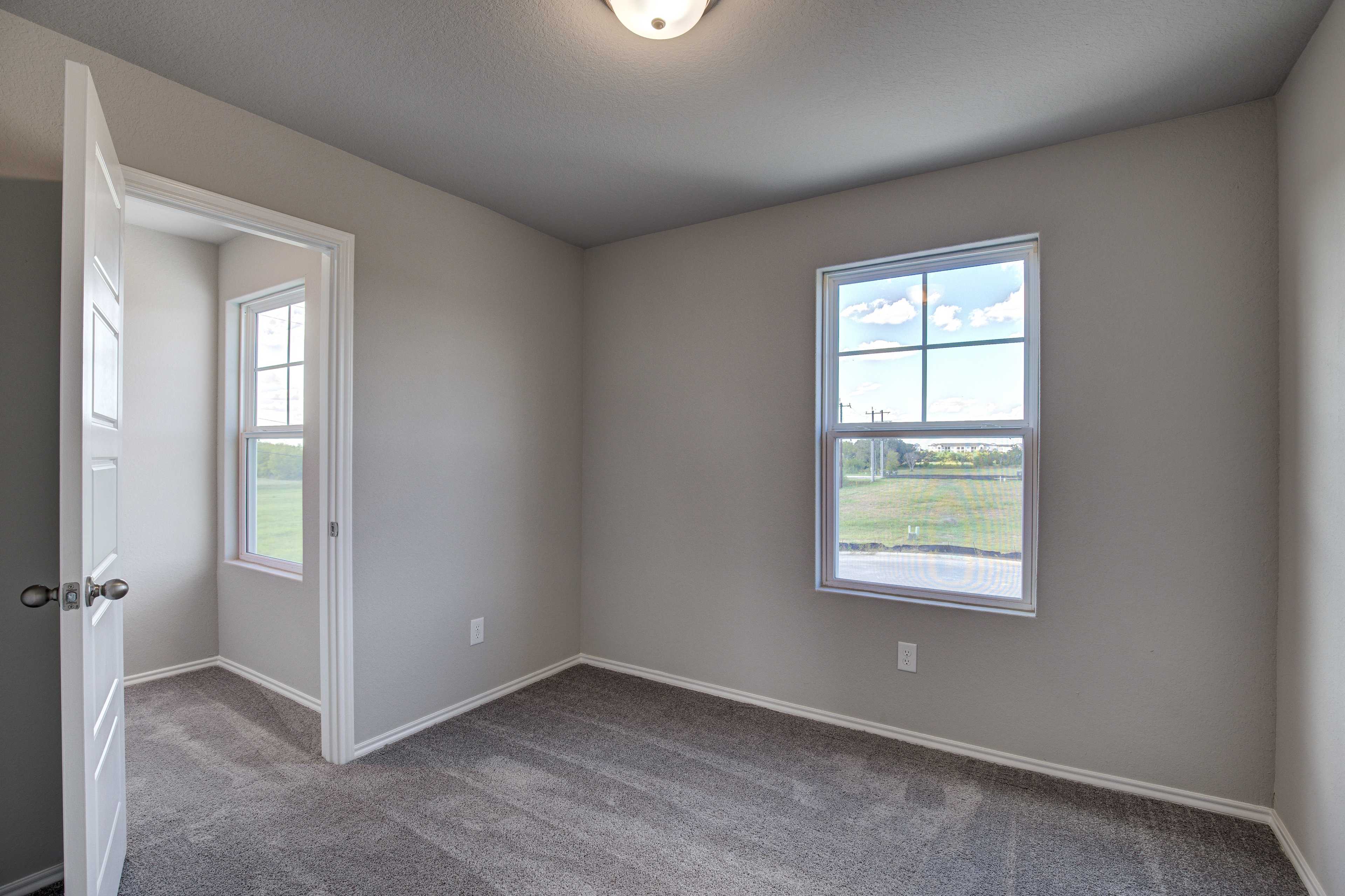 Spacious secondary bedroom in The Blanco B with neutral beige walls, carpeted floor, and large window overlooking green fields