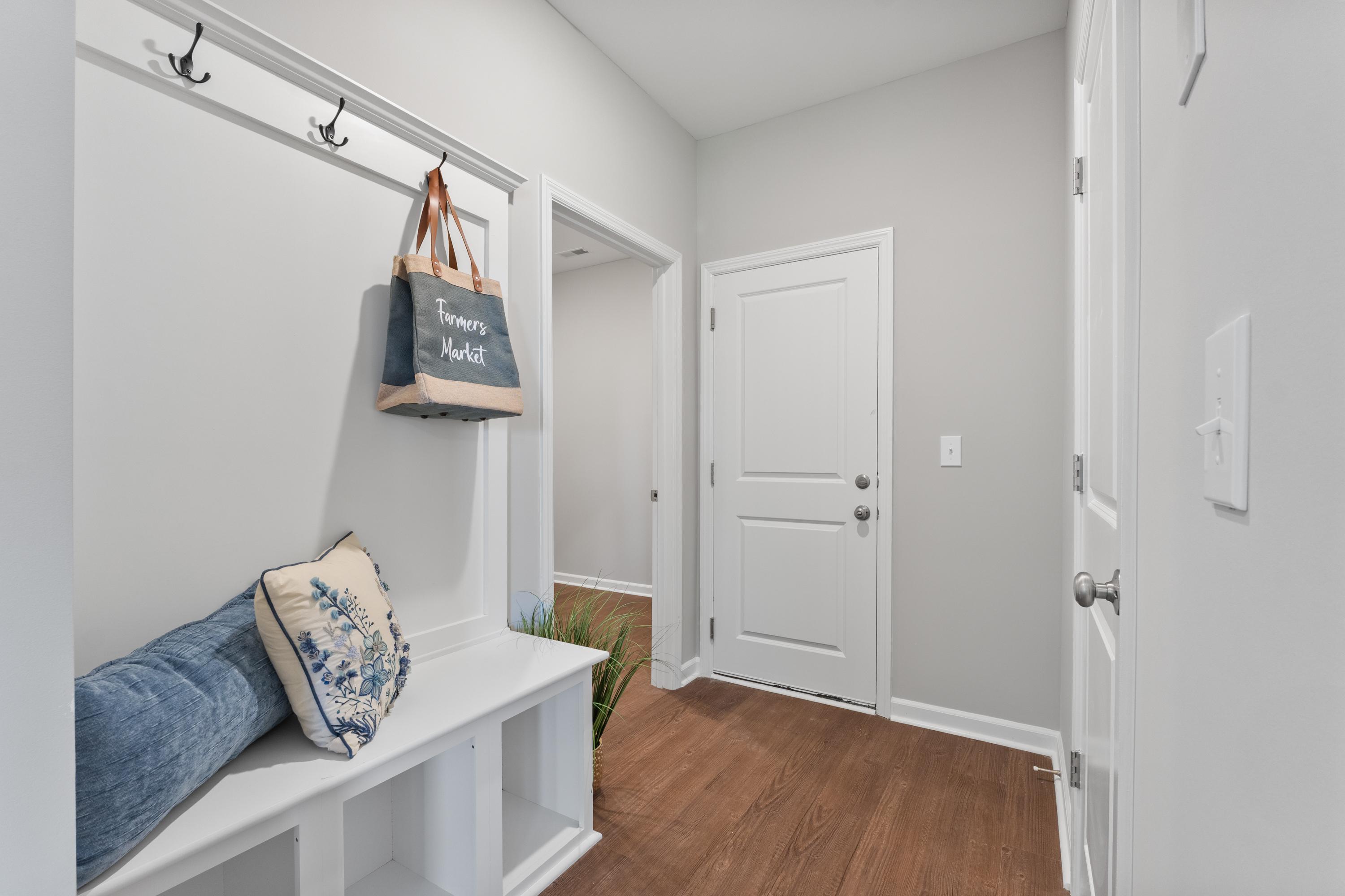 Spacious mudroom in The Avalon D home featuring built-in bench with cushions, coat hooks, hardwood floors, and neutral walls