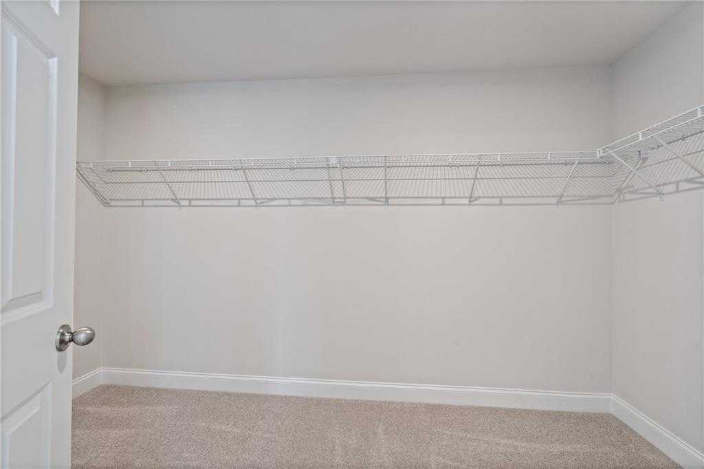 Spacious walk-in closet with white wire shelving and carpet floor in Davidson Homes The Hickory B at Wehunt Meadows, Hoschton, Georgia