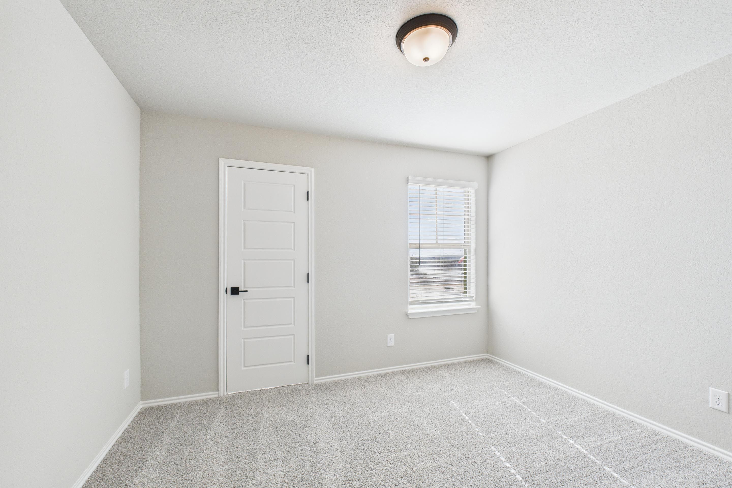 Bright, carpeted bedroom in The Charlotte floor plan by Davidson Homes featuring neutral walls and a window with blinds.